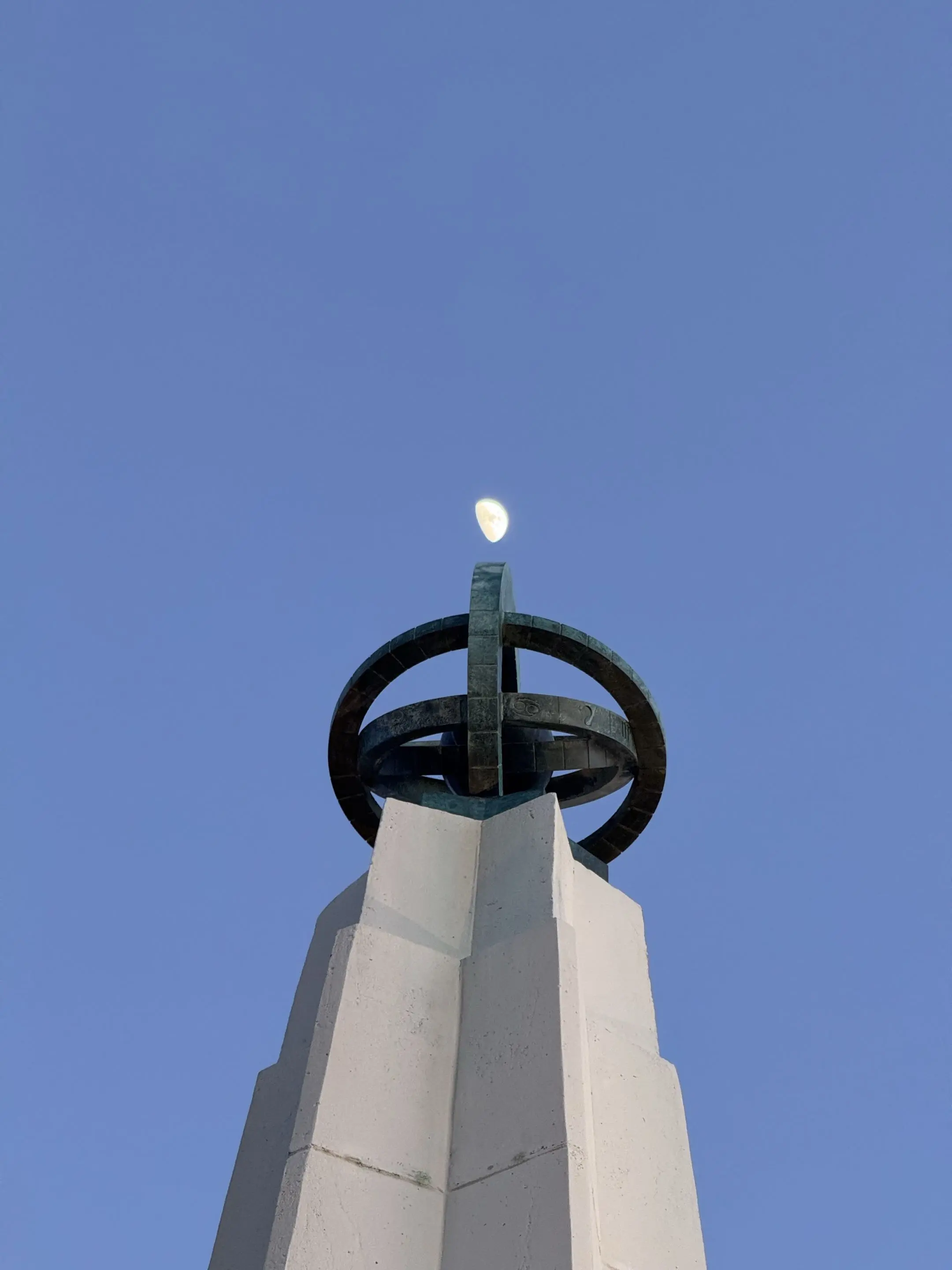 Griffith Observatory at dusk with the moon balanced at the tip of its spire.