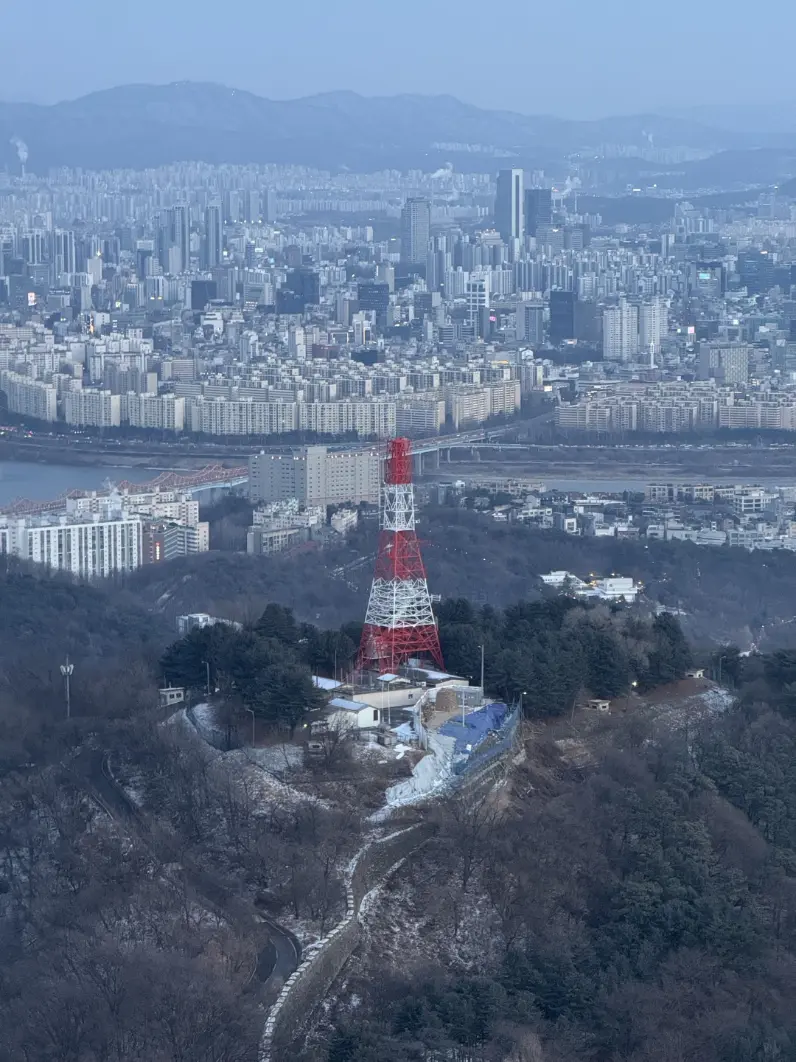 A red-and-white radio tower crowning a misty blue mountain above the city.