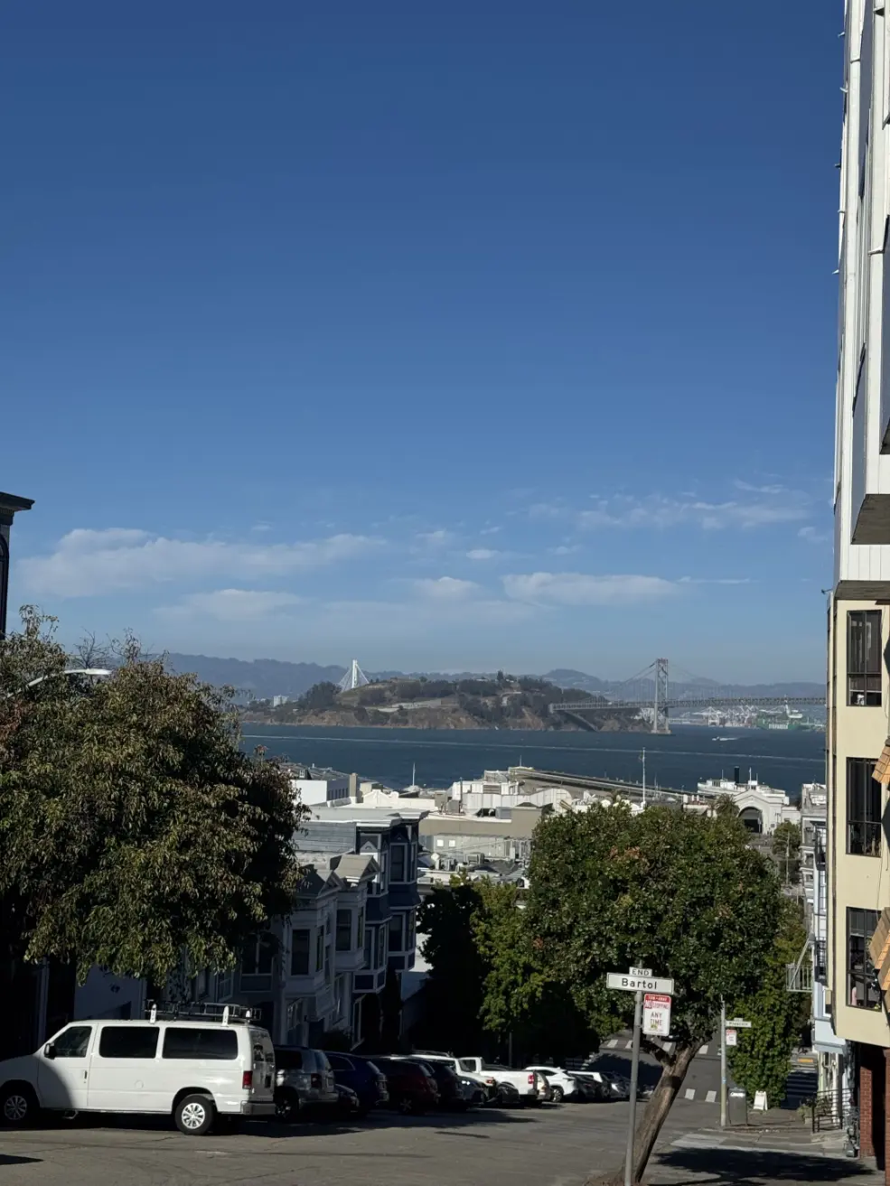 A San Francisco street dropping toward the bay, the ocean and an island in view.